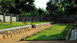 A landscaped garden with a stone wall, small plants, and a concrete pathway. - Kandez Holiday Home (Entebbe)