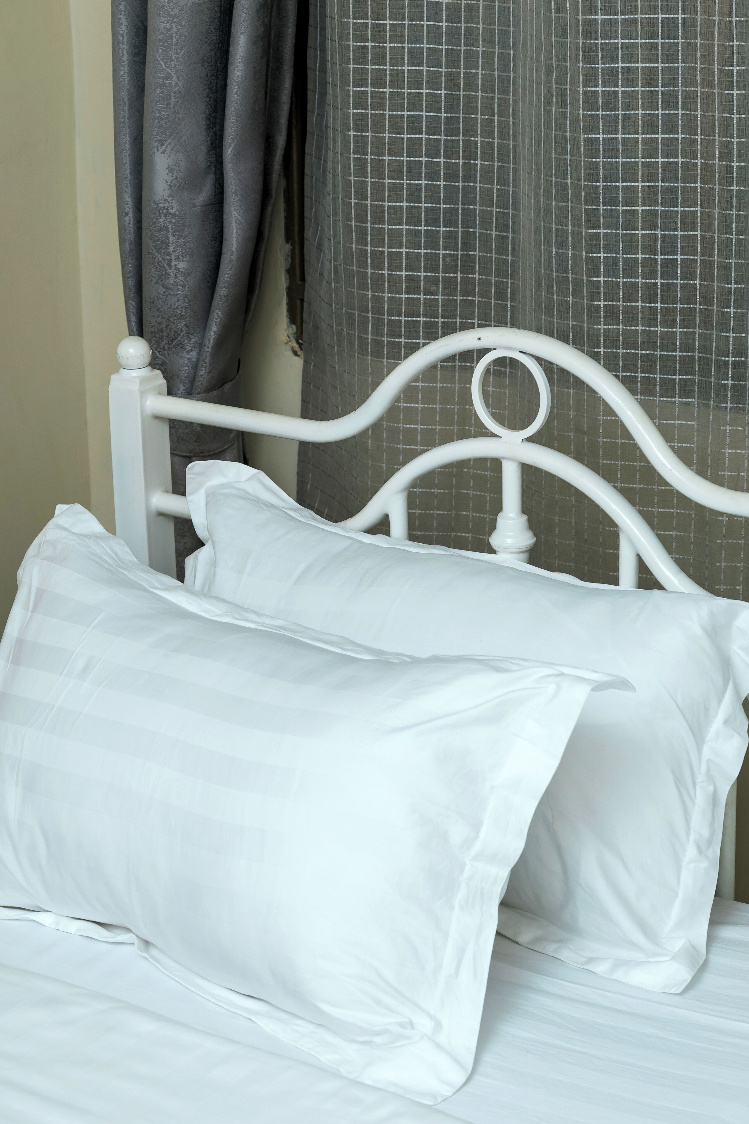 Een wit metalen bed met twee kussens en een witte lakens.