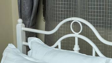 Een wit metalen bed met twee kussens en een witte lakens.