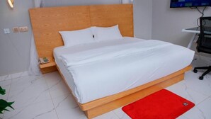 A neatly made bed with white bedding, a wooden headboard, and a red rug on a tiled floor.