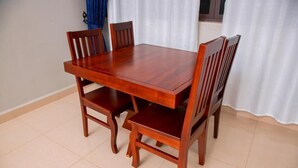 A wooden dining table with four chairs, set against a white curtain backdrop.