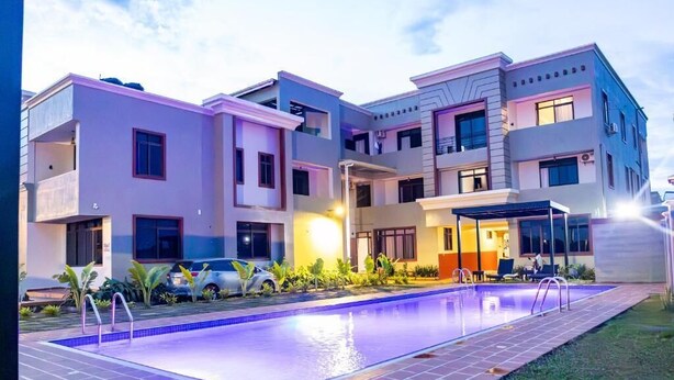 A modern multi-story residential building with a swimming pool, balconies, and a covered outdoor seating area.