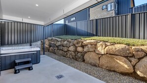 A modern outdoor hot tub area with a stone wall and a metal fence. - The Base at Abbott. Unwind with Private Spa -14 Abbott Street (Jindabyne)