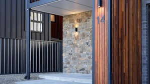 A modern building entrance with a stone wall, a wooden door, and a metal gate. - The Base at Abbott. Unwind with Private Spa -14 Abbott Street (Jindabyne)