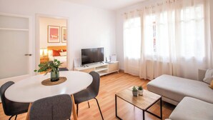 Un salon moderne doté d’un téléviseur à écran plat, d’une table à manger avec des chaises, d’un canapé et d’un ventilateur de plafond.