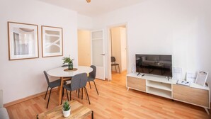 Un salon moderne avec une table à manger ronde, des chaises grises, une table basse en bois, un téléviseur posé sur un meuble blanc et un ventilateur de plafond.