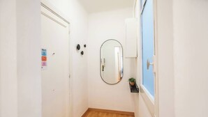 Un couloir étroit avec un plancher en bois, une porte blanche, un miroir et une fenêtre bleue.