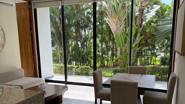 A modern kitchen with a granite countertop, a dining area with a table and chairs, and large windows offering a view of a tropical garden. - Family vacations in Tamaran (Cruz de Huanacaxtle)