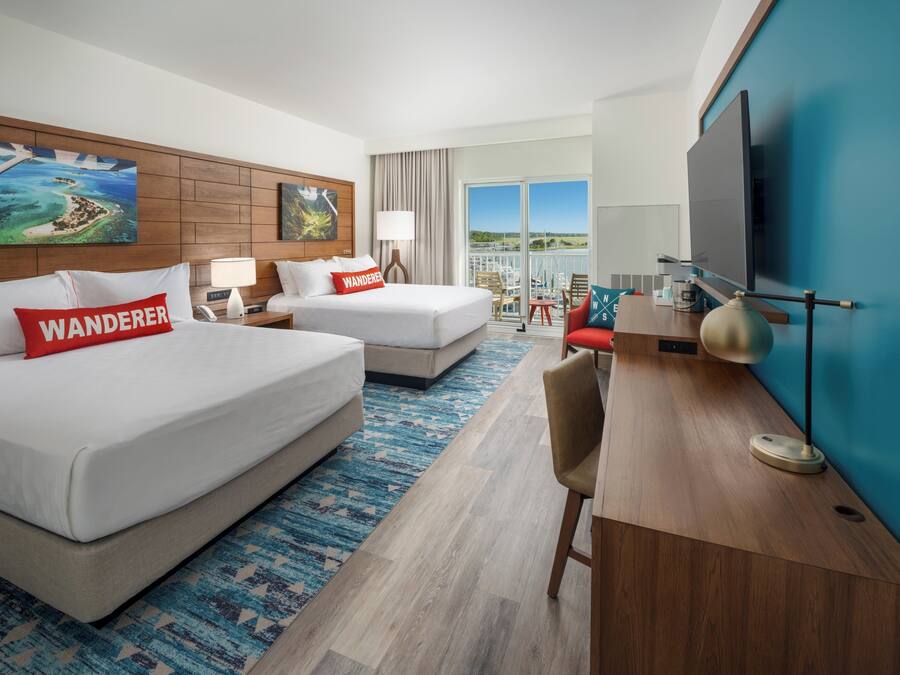 A hotel room with two beds, a desk, a TV, and a large window with a view.