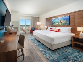 Un cuarto de hotel con una cama grande, un escritorio con televisor, una silla, una ventana con vista al puerto deportivo y un cuadro en la pared.