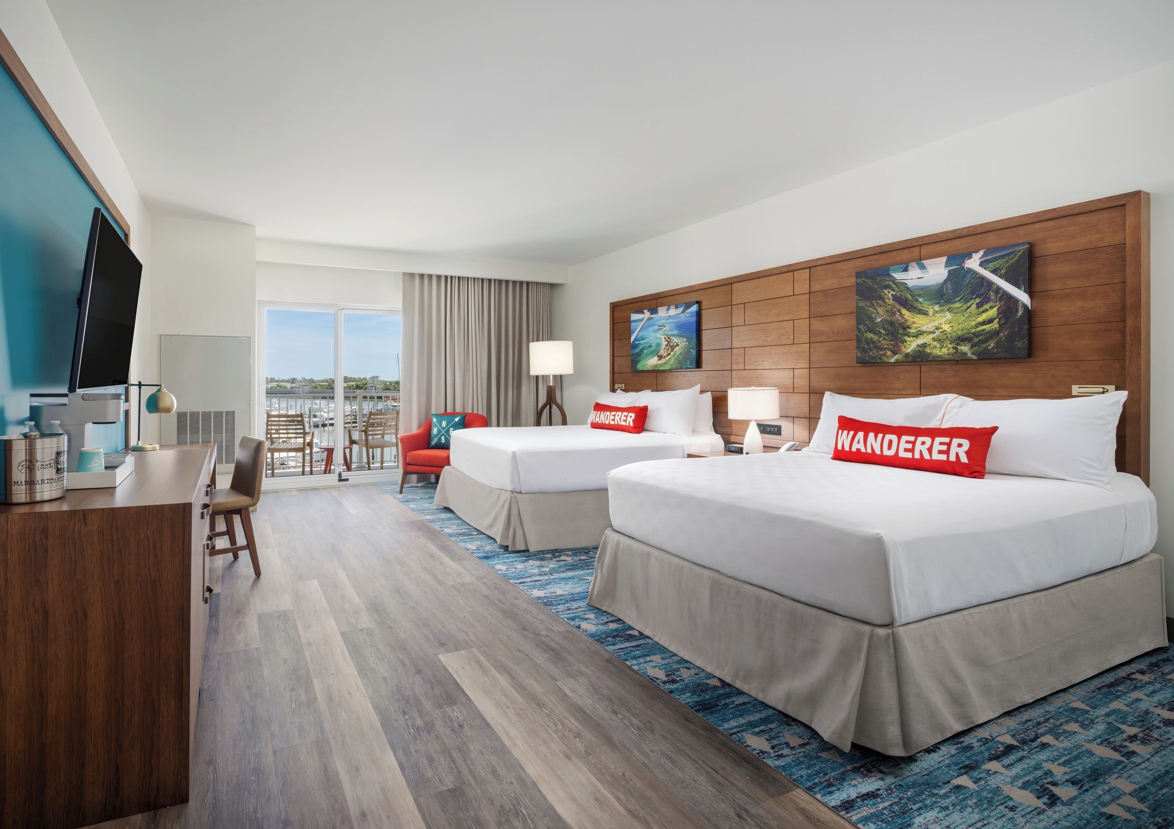 Habitación de hotel con dos camas, un escritorio, una silla, un televisor y vistas al exterior.