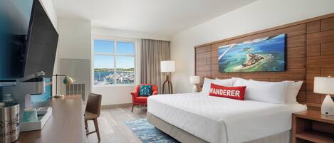 A hotel room with a bed, a desk, a chair, a television, and a window with a view of boats.