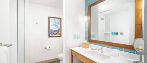 A modern bathroom with a glass shower enclosure, a wooden vanity with a large mirror, and a framed picture on the wall.
