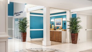 A modern hotel lobby with a compass floor design, a meeting room, and potted plants. - Compass by Margaritaville Beaufort (Beaufort)