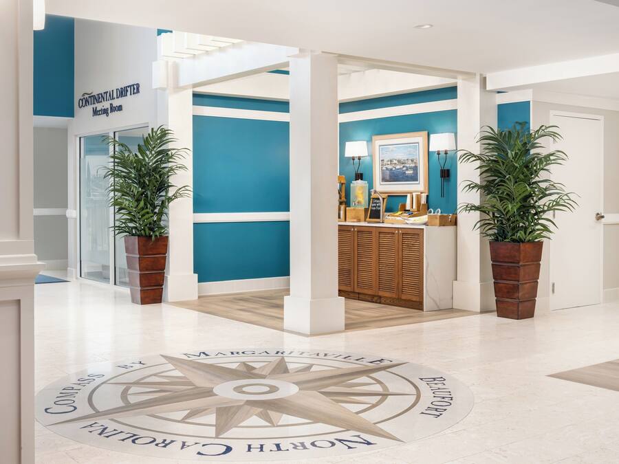 Un hall d’hôtel moderne avec un motif de boussole sur le sol, une salle de réunion et des plantes en pot.