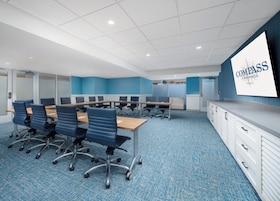 A conference room with a long table, chairs, a whiteboard, and a blue carpet.