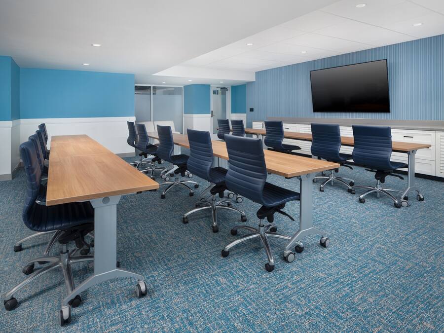 A conference room with a long table, multiple chairs, a flat-screen TV, and a blue-striped wall.
