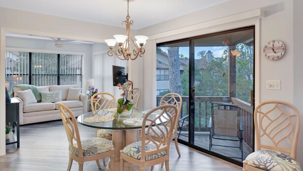 A dining area with a glass table, wooden chairs, and a chandelier. - Nice 3 bedroom condo located in Harbour Oaks (Saint Simons Island)
