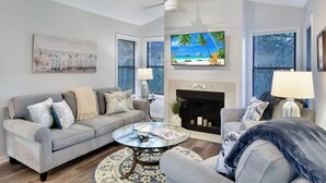 A living room with a grey sofa, a glass coffee table, a fireplace, and a TV mounted above it. - Nice 3 bedroom condo located in Harbour Oaks (Saint Simons Island)
