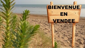 A wooden welcome sign with the text "BIENVENUE EN VENDEE" on a beach.