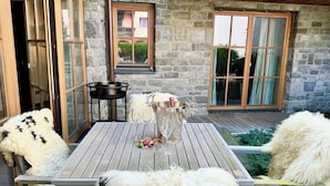 A stone building with a wooden deck, a table with chairs, and a decorative metal container. - Exclusive deluxe suite in the heart of Kitzbühel (Kitzbühel)