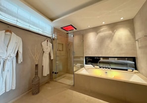 A modern bathroom with a large bathtub, a glass shower enclosure, and two white robes hanging on the wall.