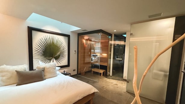 A modern bedroom with a large bed, a framed artwork, a wooden bench, and a glass door leading to a bathroom. - Exclusive deluxe suite in the heart of Kitzbühel (Kitzbühel)