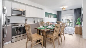 A modern kitchen with stainless steel appliances, a dining table set with green placemats, and wooden chairs.