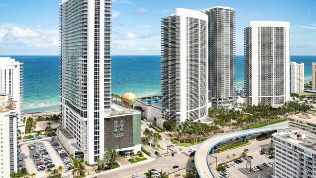 A high-rise hotel with multiple floors, a parking lot, and a view of the ocean.