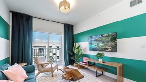 A modern living room with a teal and white color scheme, a large window, a sofa, a coffee table, a TV, and a plant.