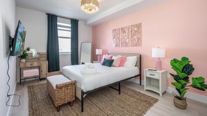 A modern bedroom with a bed, bedside tables, a dresser, a mirror, and a large potted plant.