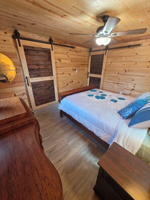 A wooden-paneled room with a bed, a ceiling fan, and a wooden nightstand.