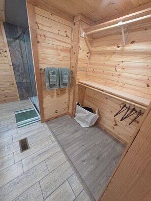 A wooden interior with a built-in bench, a towel rack with two towels, a hanging clothes rack, and a small trash bin.