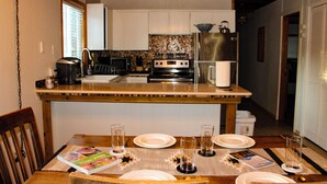 Une cuisine avec des meubles blancs, un réfrigérateur en acier inoxydable et un four à micro-ondes. On y trouve une table à manger mise avec des assiettes, des verres et un livre de recettes.