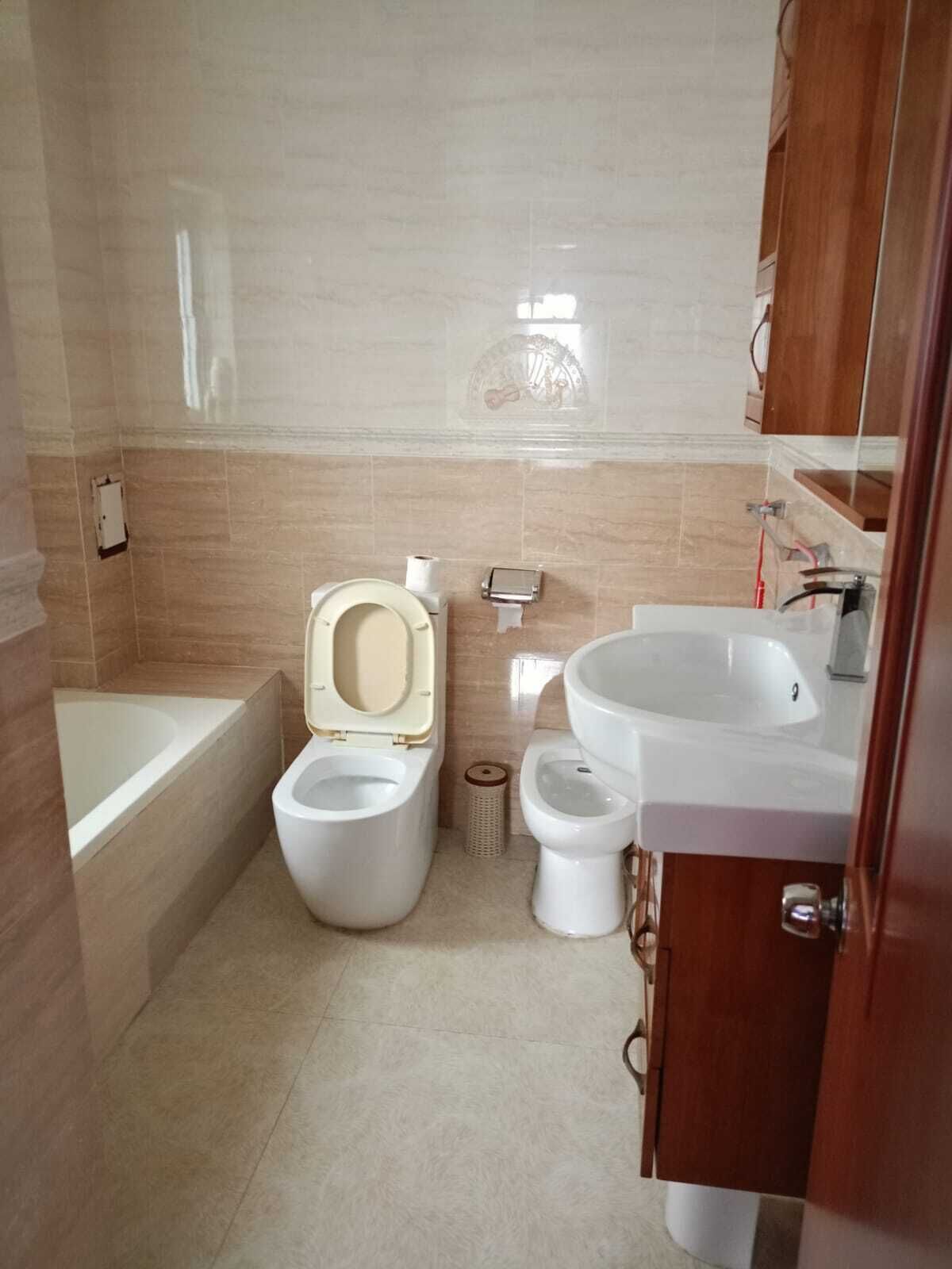 Een badkamer met een badkuip, twee toiletten, een wastafel en een spiegel.