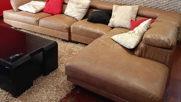 A living room with a brown leather sofa, a black coffee table, and a red accent wall. - Luanda, Angola! Next to the Multipurpose Pavilhao! Centralidade do Kilamba, block M15 (Kilamba)