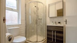 A bathroom with a glass shower enclosure, a toilet, a sink with a mirror, and a window. - Ideal for Contractors | Free Wi-Fi | Sleeps 7! (Northampton)