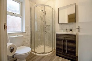 Ein Badezimmer mit Duschkabine, Toilette, Waschbecken und Spiegel sowie einem Fenster.