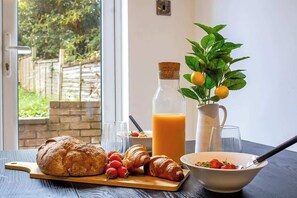 Ein Frühstückstisch mit Brot, Croissants, Erdbeeren, einem Glas Orangensaft und einer Saftkanne.