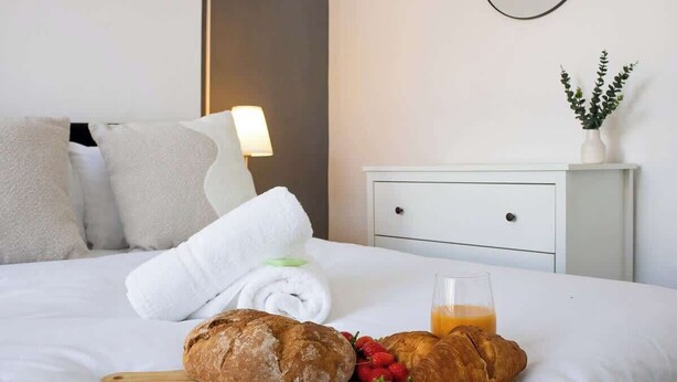 A neatly made bed with a rolled white towel, a loaf of bread, a croissant, strawberries, and a glass of orange juice. - Ideal for Contractors | Free Wi-Fi | Sleeps 7! (Northampton)