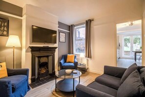 Ein Wohnzimmer mit Kamin, Fernseher, Sofa und Sessel.
