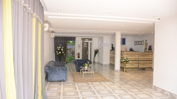 A hotel lobby with a reception desk, two sofas, a coffee table, and a patterned floor. - Hunters Royal Apartments (Madina)