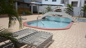 A swimming pool with a tiled deck, lounge chairs, and a staircase leading to a building. - Hunters Royal Apartments (Madina)