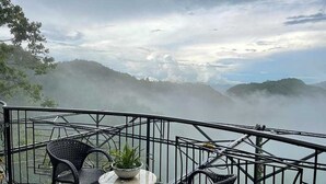 A balcony with two wicker chairs and a small table, overlooking misty mountains. - OYO 1173 Sermon On The Mount Retreat (Balamban)