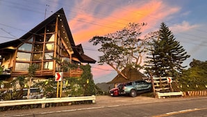 A building with a sloped roof and large windows, situated next to a road with cars parked. - OYO 1173 Sermon On The Mount Retreat (Balamban)