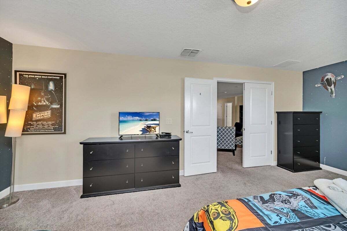 Ein Schlafzimmer mit einem Bett, einem Schminktisch, einem Fernseher und einem Bild an der Wand.