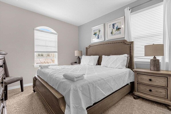 A bedroom with a large bed, a nightstand, a dresser, and a window with blinds.