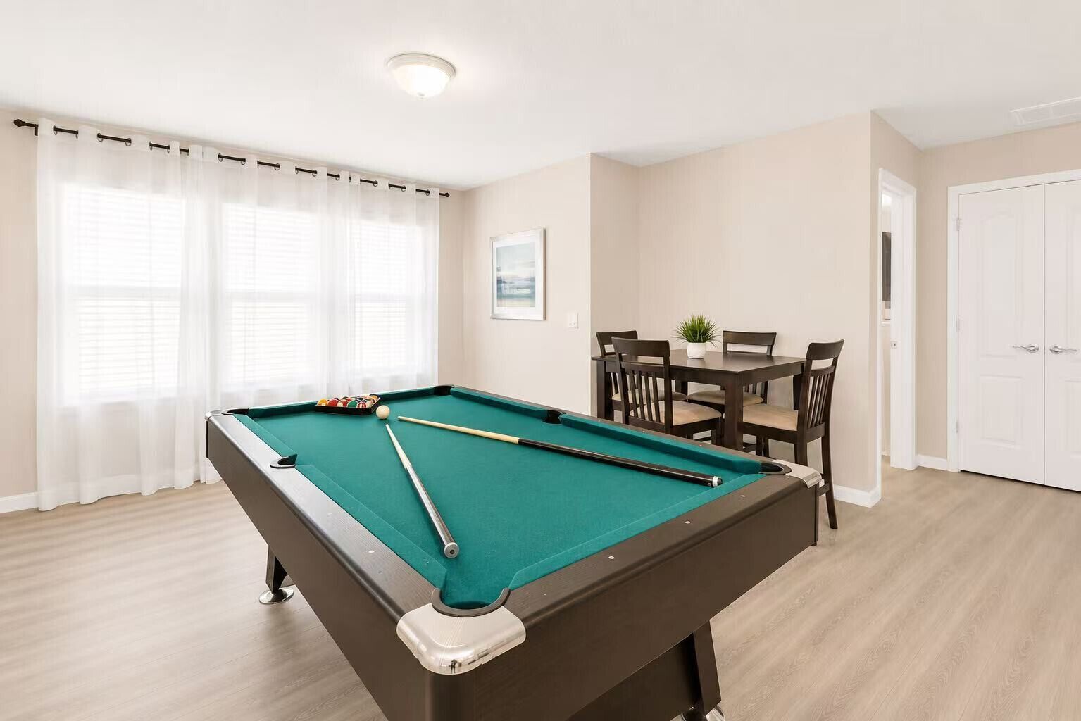 A pool table with a green felt surface, a white door, and a dining area with a table and chairs.