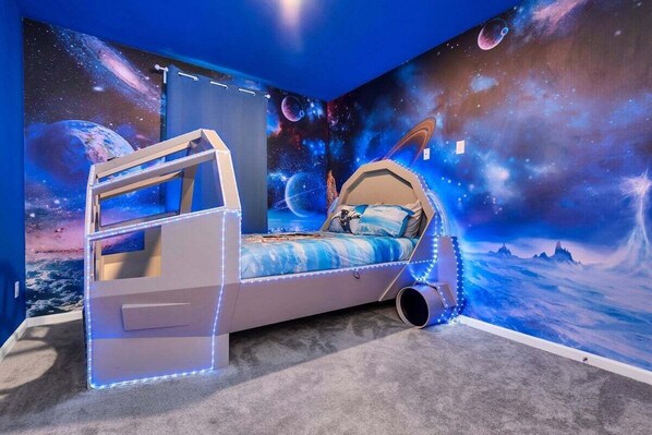 A bedroom with a space-themed mural, a bed with a canopy, and a desk with a chair.