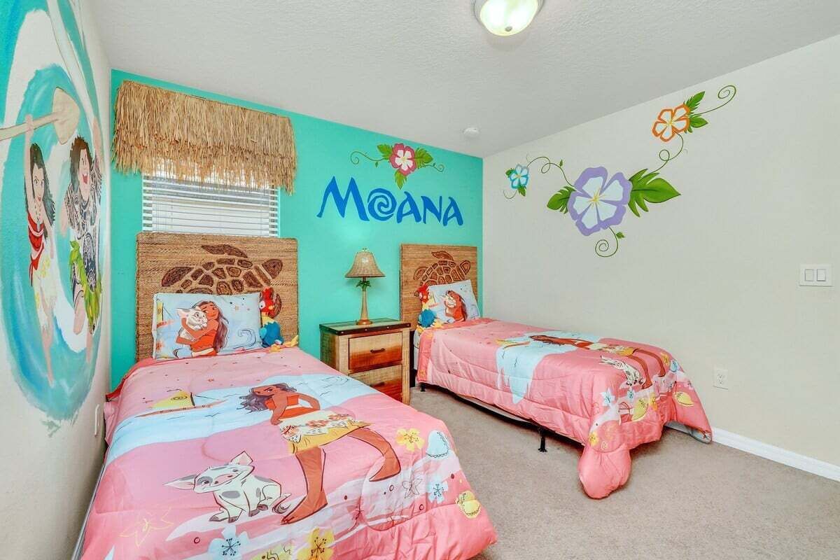 Una habitación con dos camas, un mural que lleva el nombre 'MOANA' y una decoración floral en la pared.